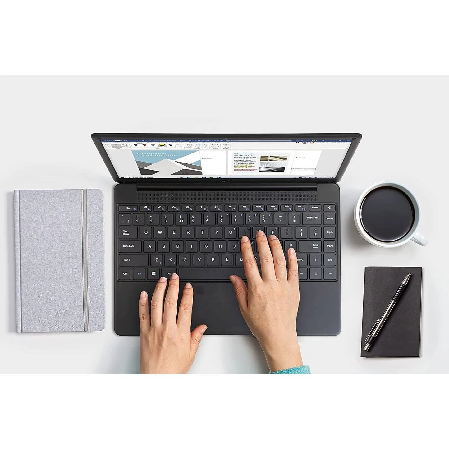 Person using a laptop with a notebook, pen, and coffee cup on a white surface