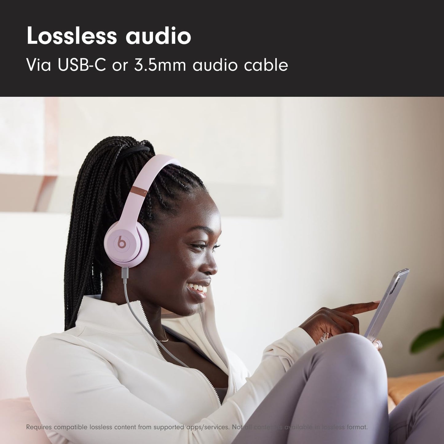 Woman wearing pink headphones, using a tablet, with text about lossless audio via USB-C or 3.5mm cable.
