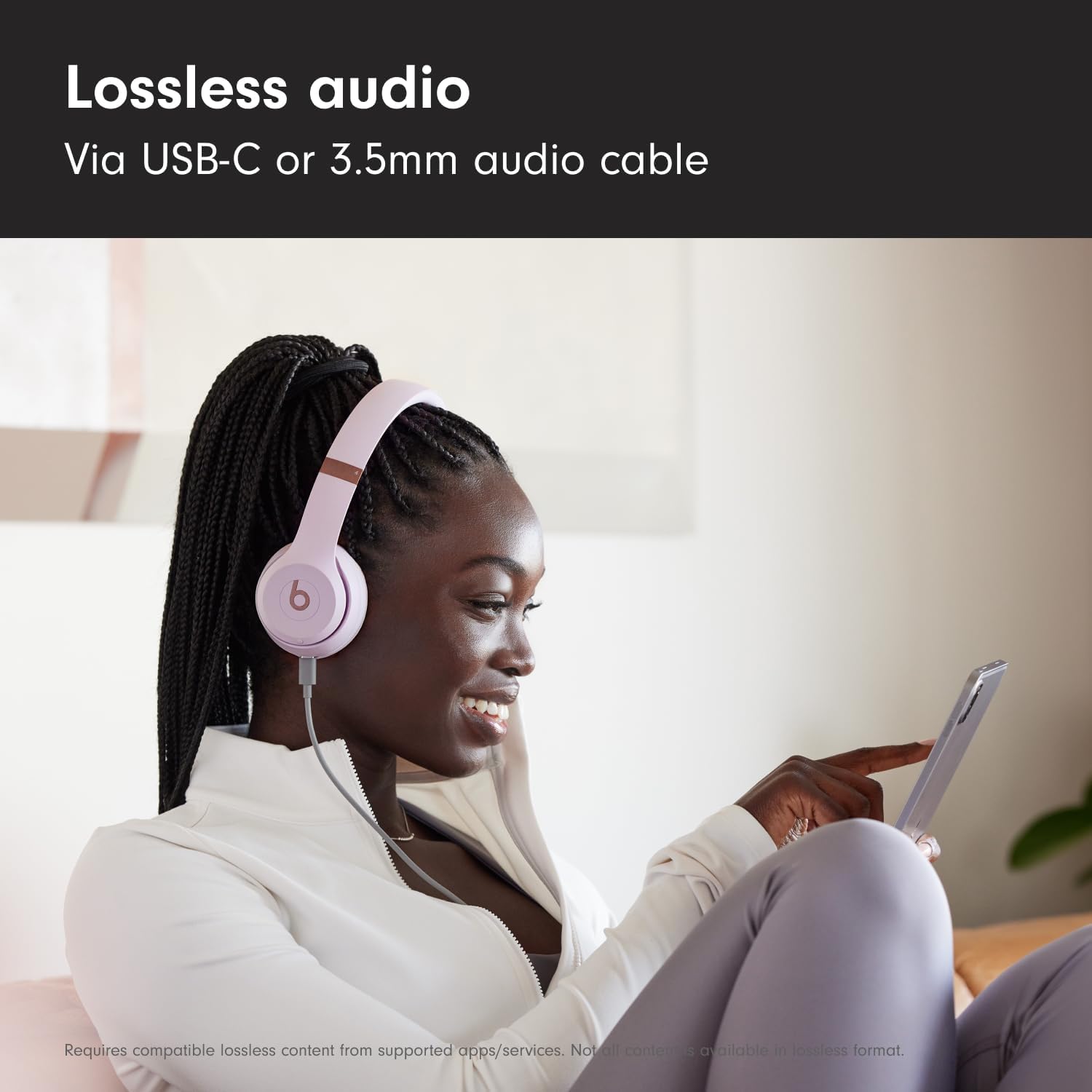 Woman wearing pink headphones, using a tablet, with text about lossless audio via USB-C or 3.5mm cable.