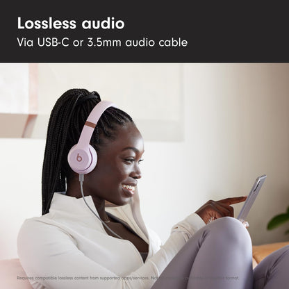 Woman wearing pink headphones, using a tablet, with text about lossless audio via USB-C or 3.5mm cable.