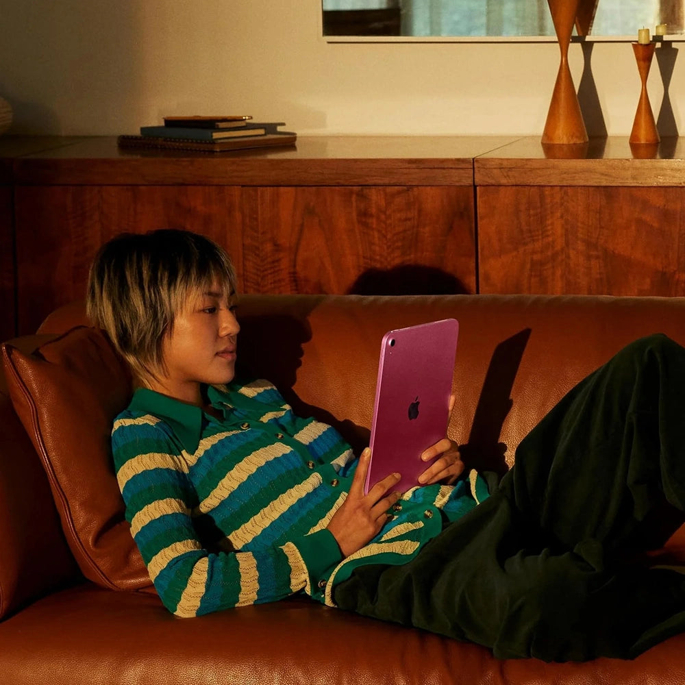Person sitting on a couch using a pink tablet in a home setting.